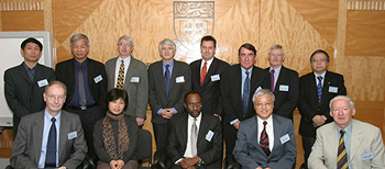 A group of 13 attendees in business attire poses for a group photograph in front of a wooden panel wall featuring the carved HKU coat of arms.